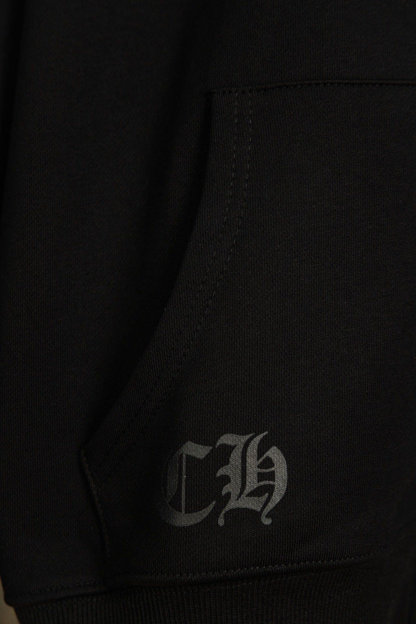 Black hoodie inner seam with stitched label; small signature graphic.