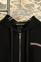 Black zip-up hoodie close-up of hood and metal front zipper; logo patch on chest.