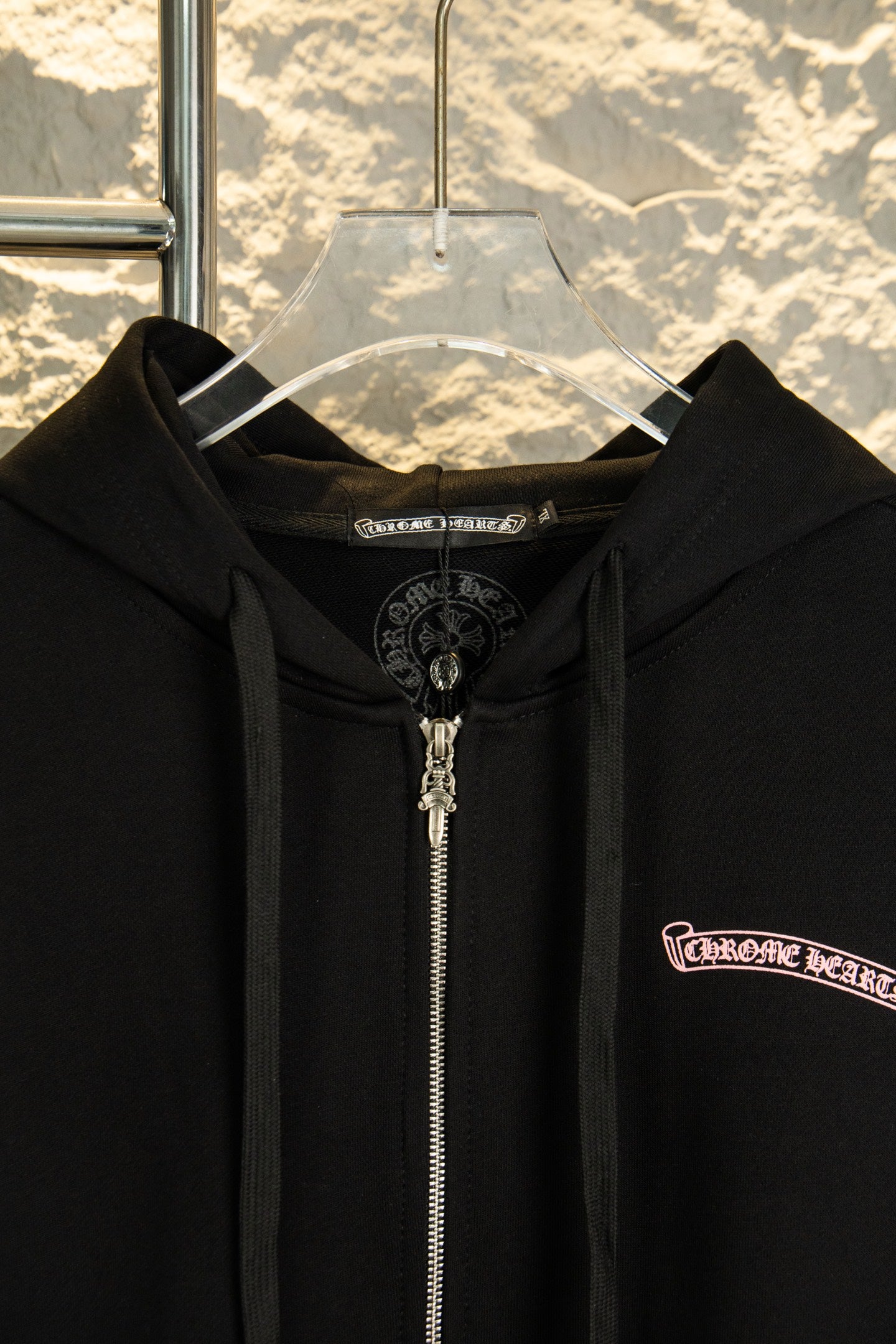 Black zip-up hoodie close-up of hood and metal front zipper; logo patch on chest.