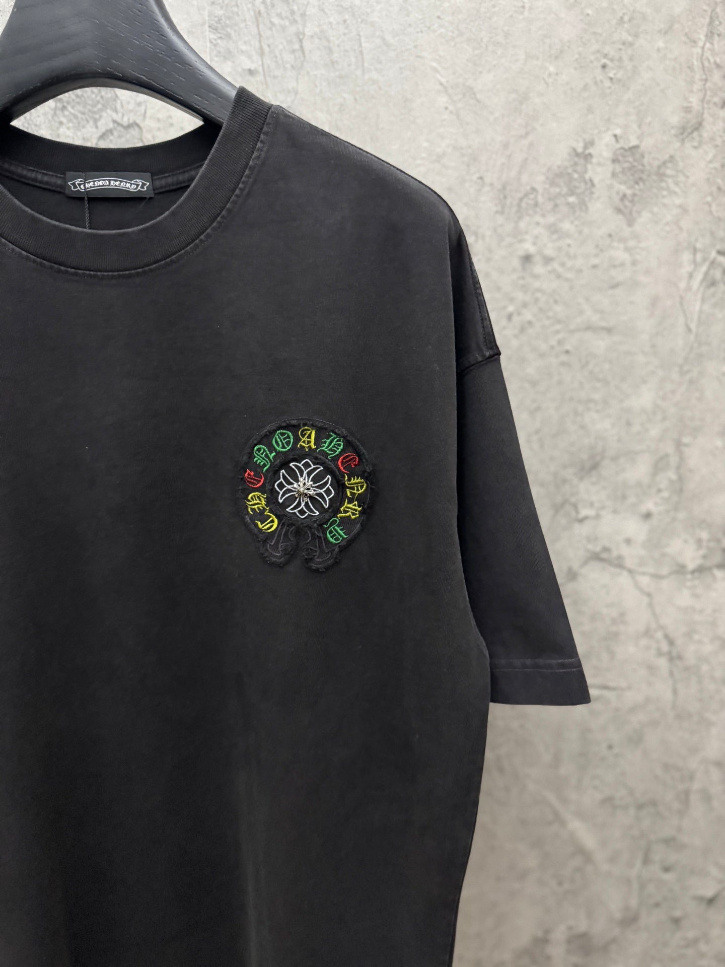 Black short-sleeve T-shirt with small multicolor circular chest embroidery.