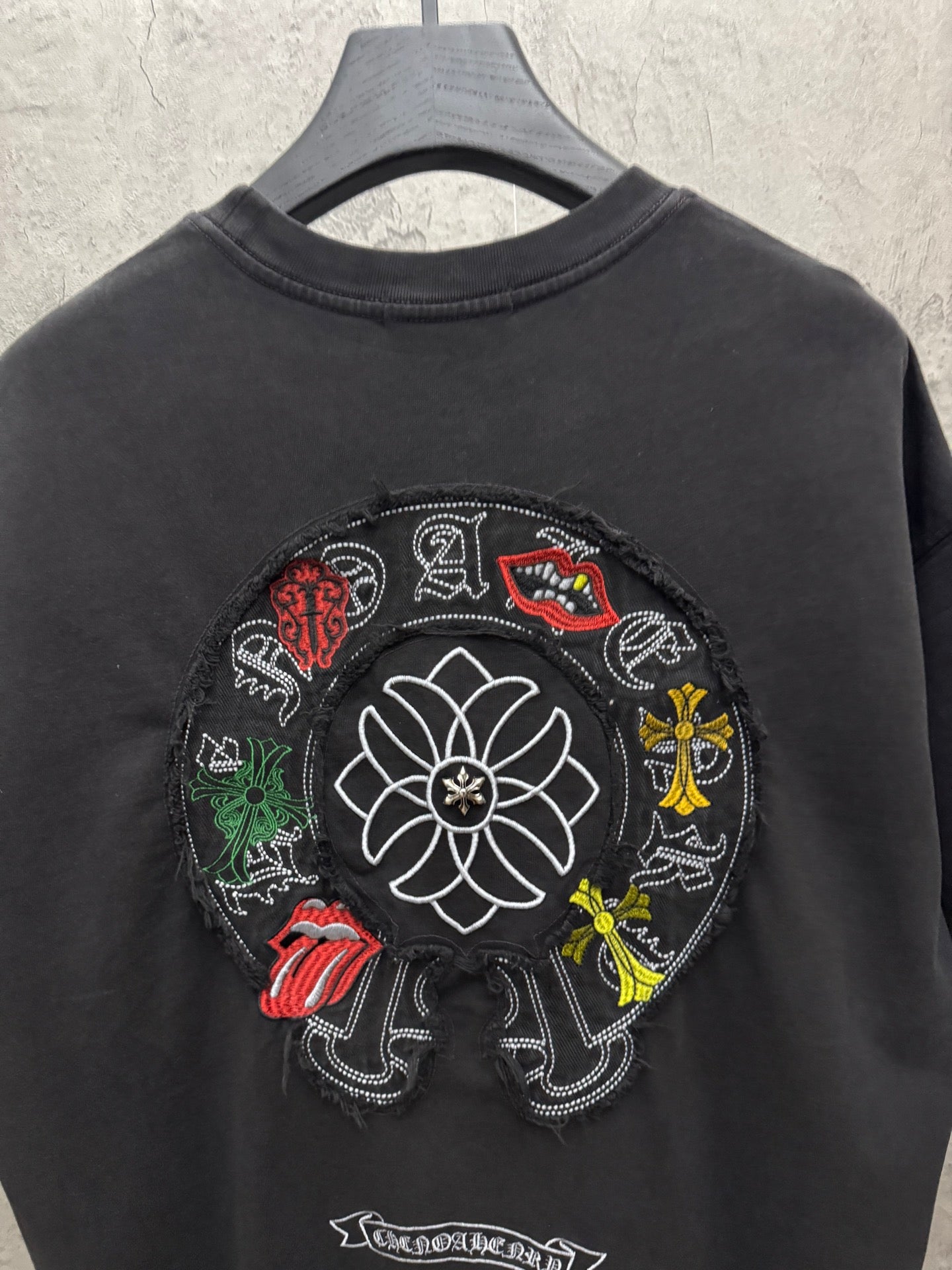 Black T-shirt back view with circular flower and character embroidery, small text patch.