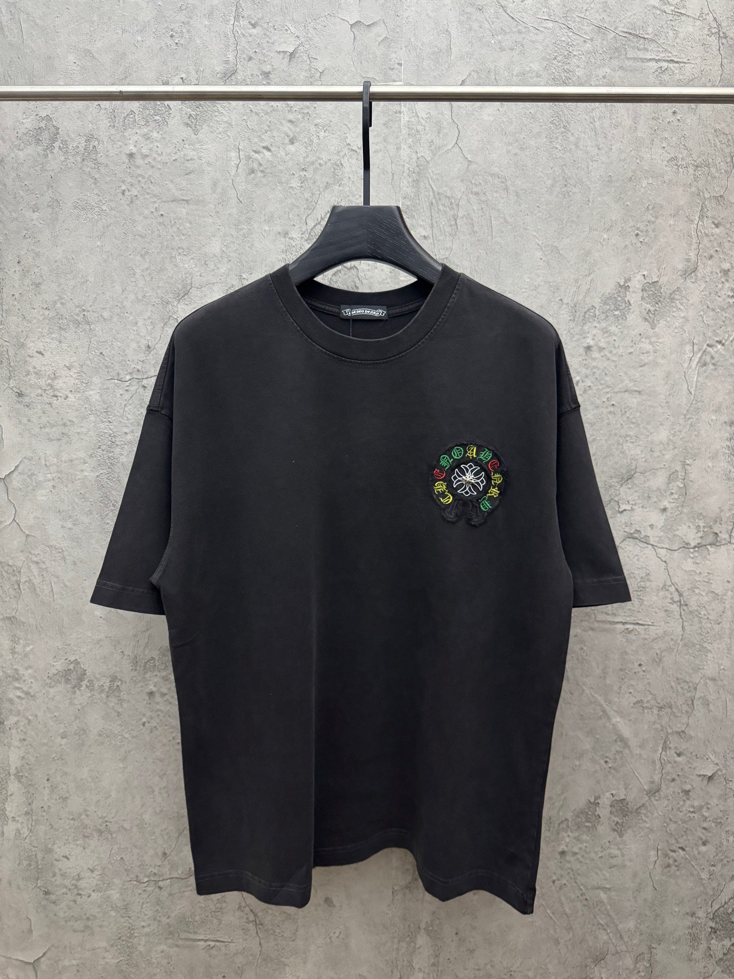 Black crewneck short-sleeve T-shirt on hanger, small multicolor chest embroidery.