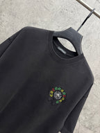 Black crewneck T-shirt close-up with small multicolor flower logo embroidery.