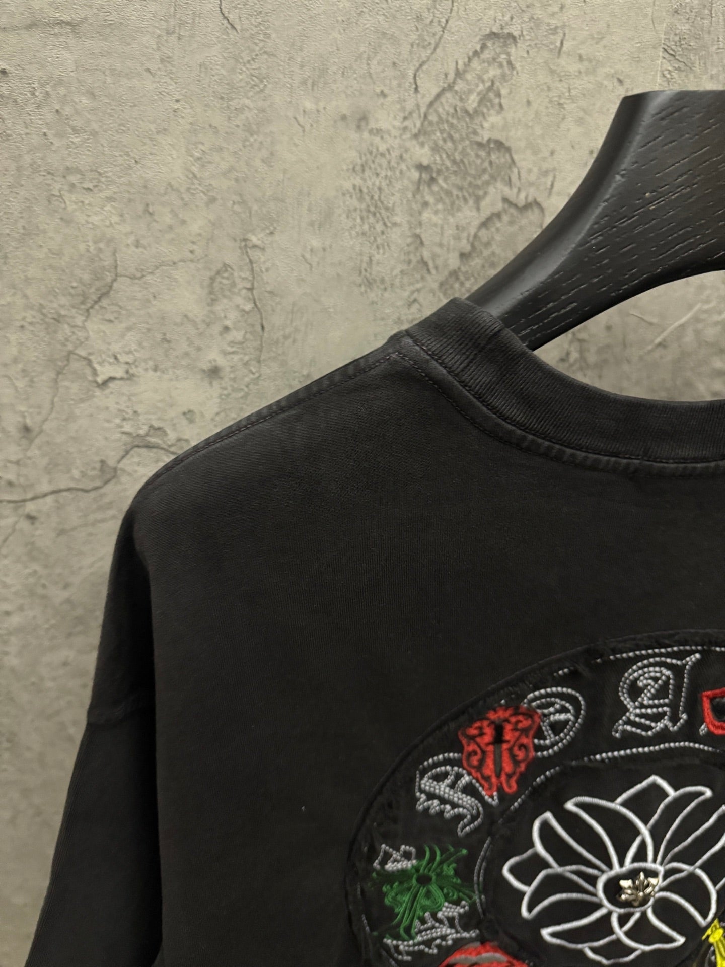 Black T-shirt shoulder with part of white flower embroidery and multicolor accents.