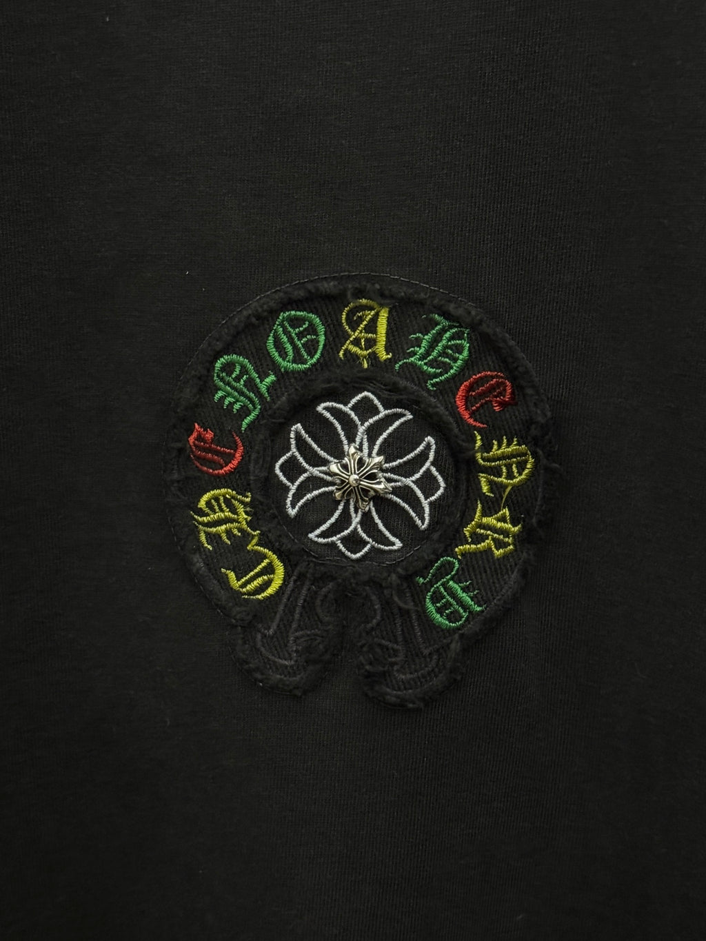 Black fabric close-up of white flower logo with multicolor stitched accents.