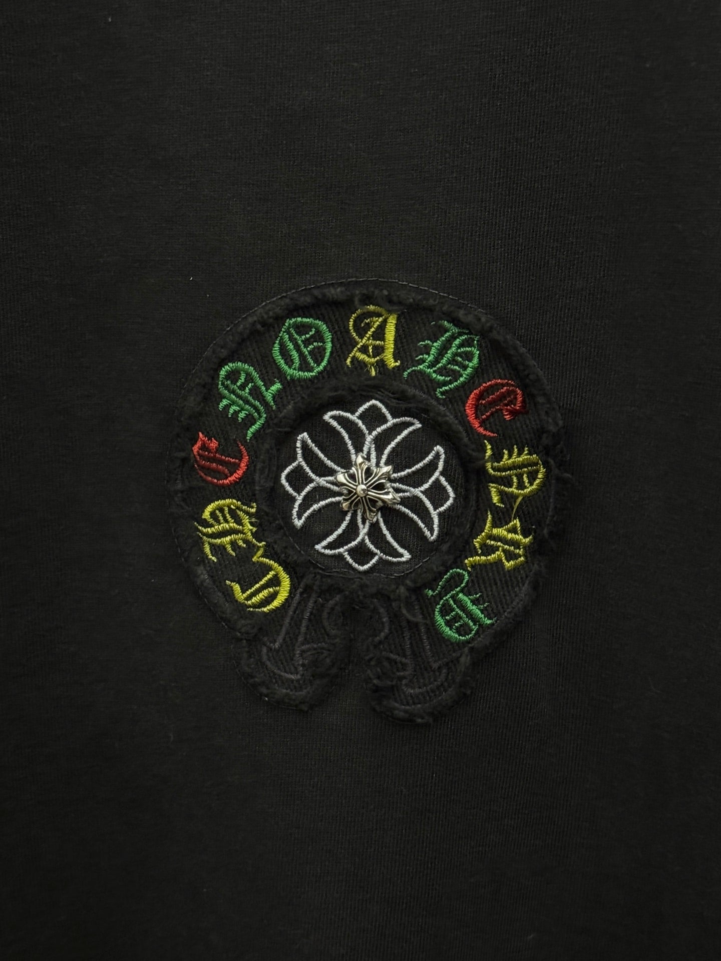 Black fabric close-up of white flower logo with multicolor stitched accents.