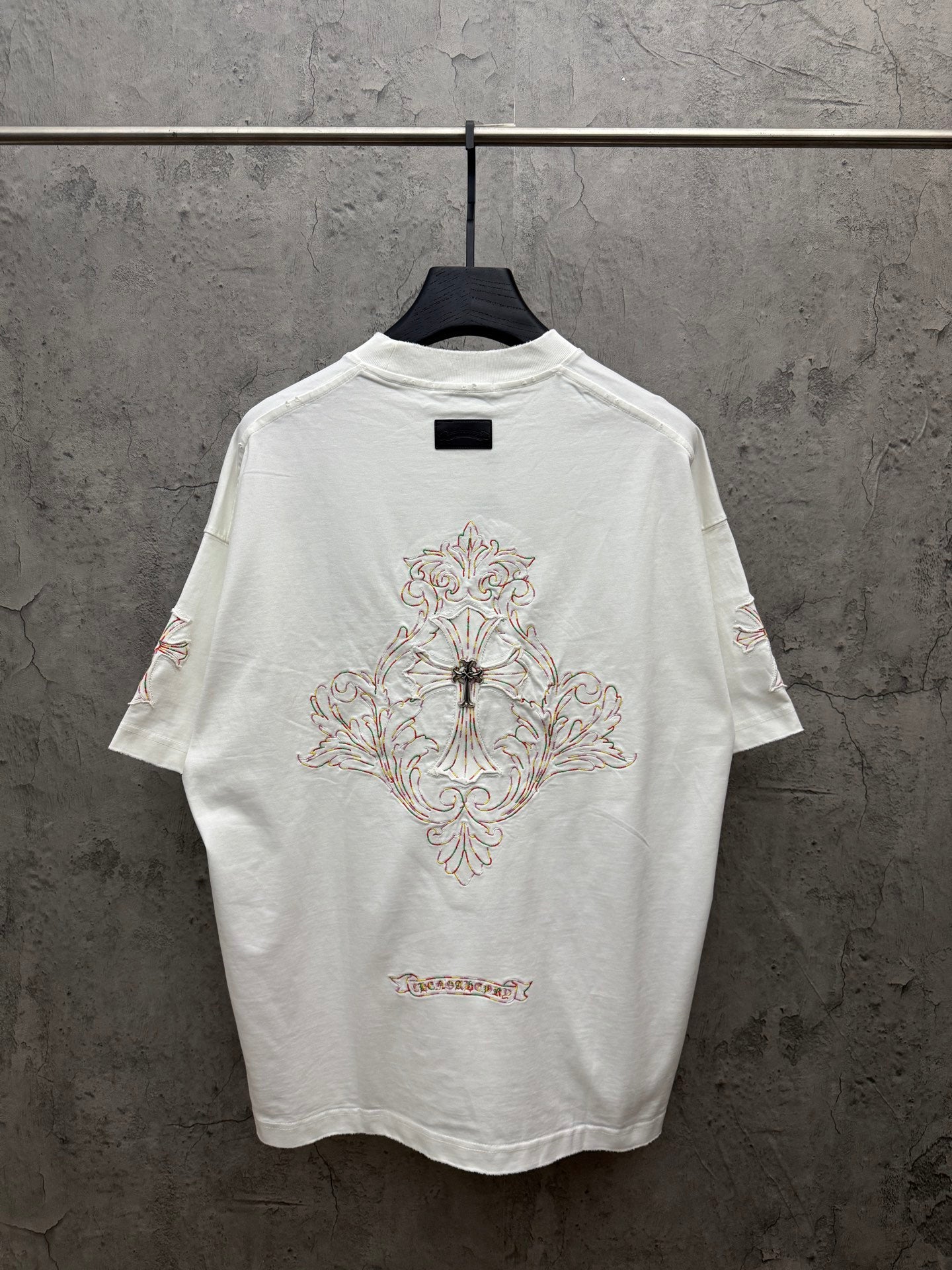 White short-sleeve T-shirt with large back cross embroidery and decorative script at hem