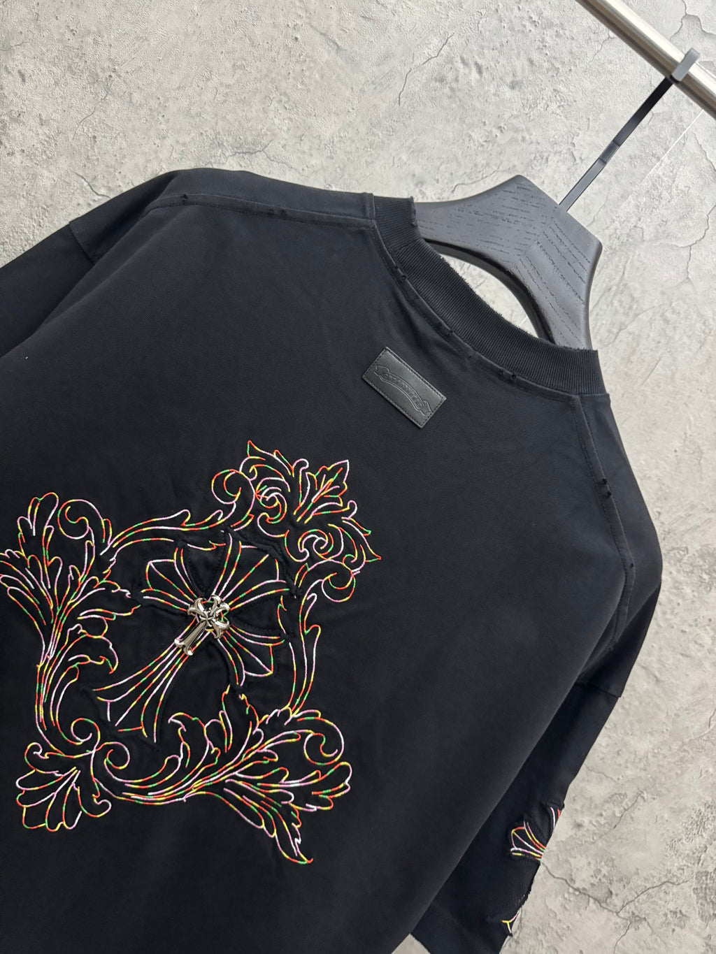 Black short-sleeve T-shirt with large floral cross embroidery and tag at collar
