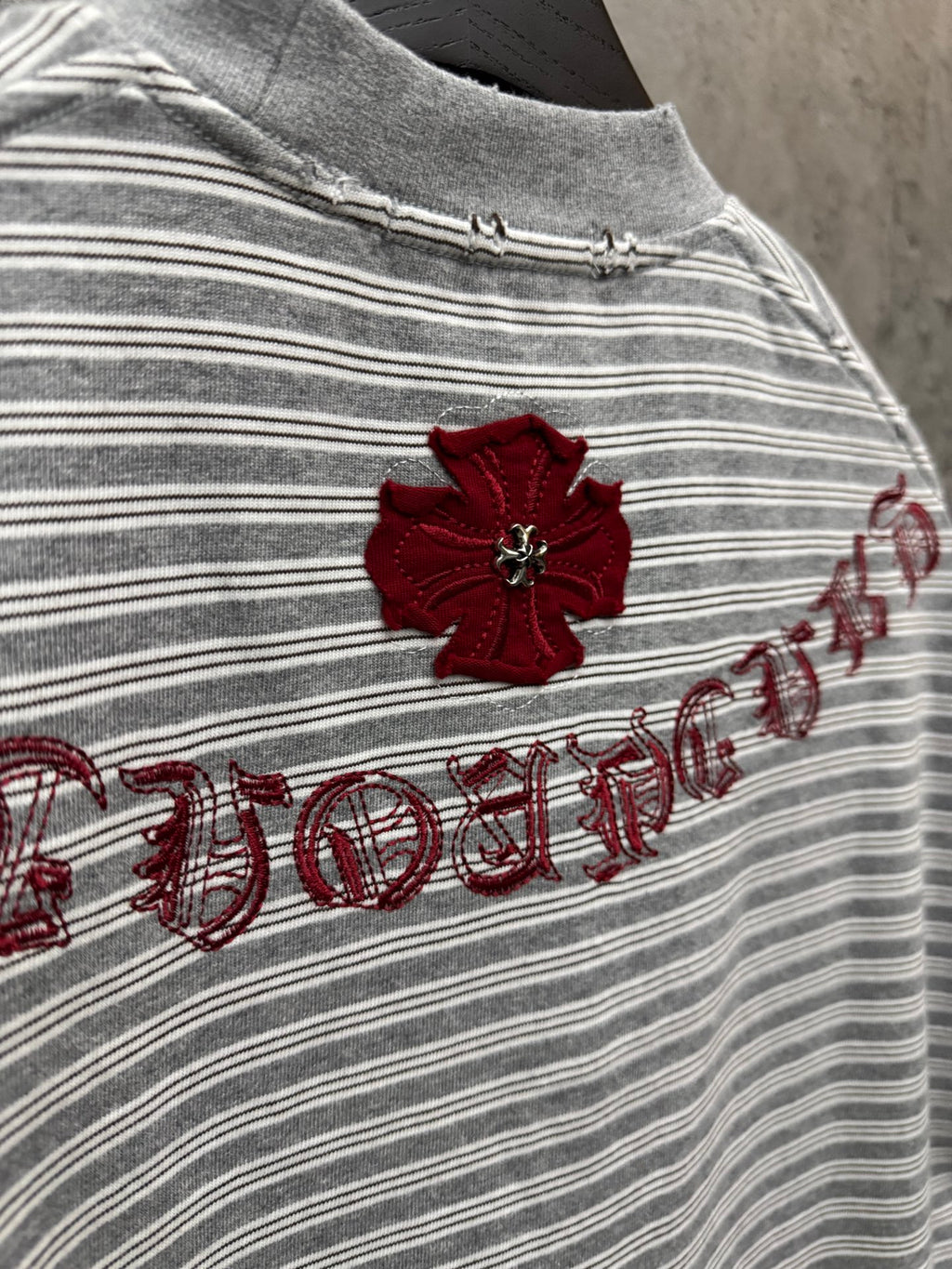 Close-up of striped short-sleeve T-shirt with red flower embroidery and script.