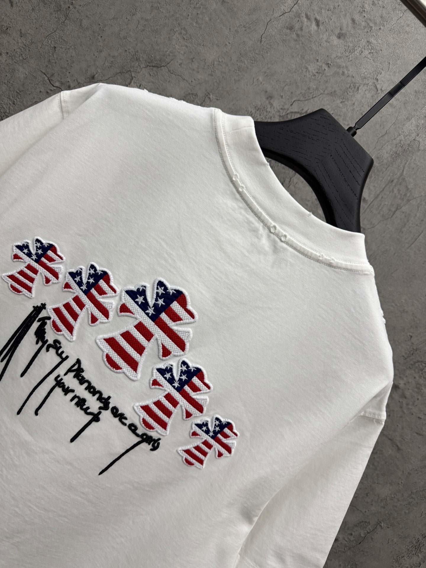 White T-shirt detail with multicolor patriotic drips and winged figure embroidery