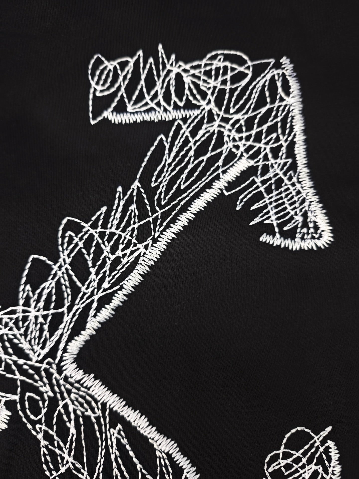 Black T-shirt close-up of white line-art graphic letterforms and shapes