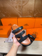 Hermes dark leather slide sandals with double cross straps, shown in hand