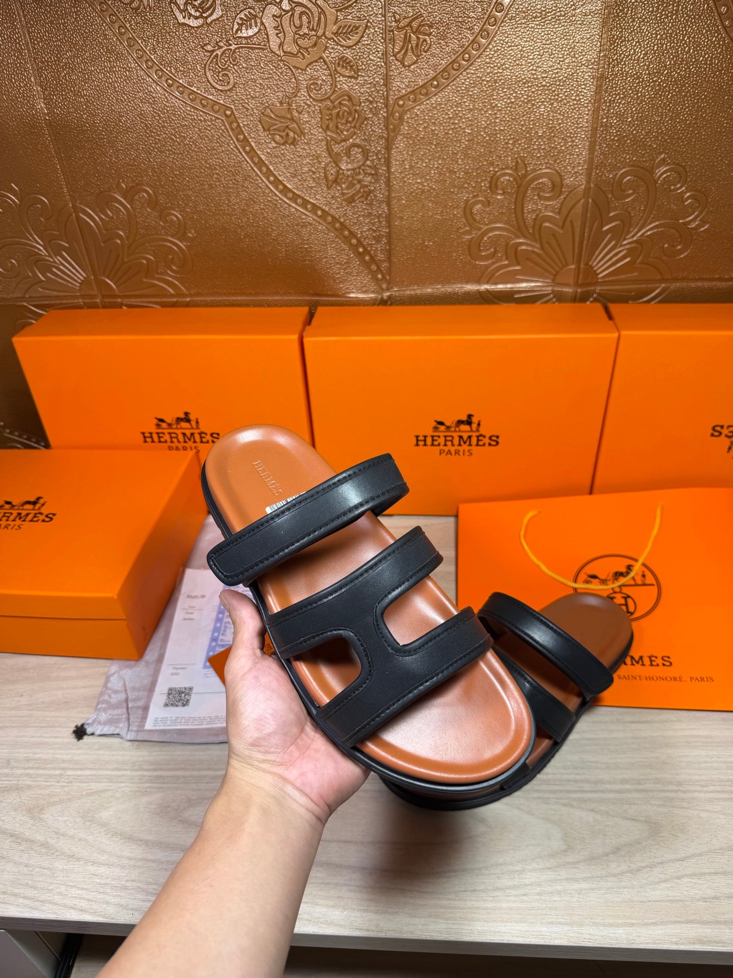 Hermes dark leather slide sandals with double cross straps, shown in hand