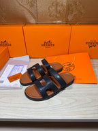 Hermes dark leather slide sandals with layered strap bands across foot