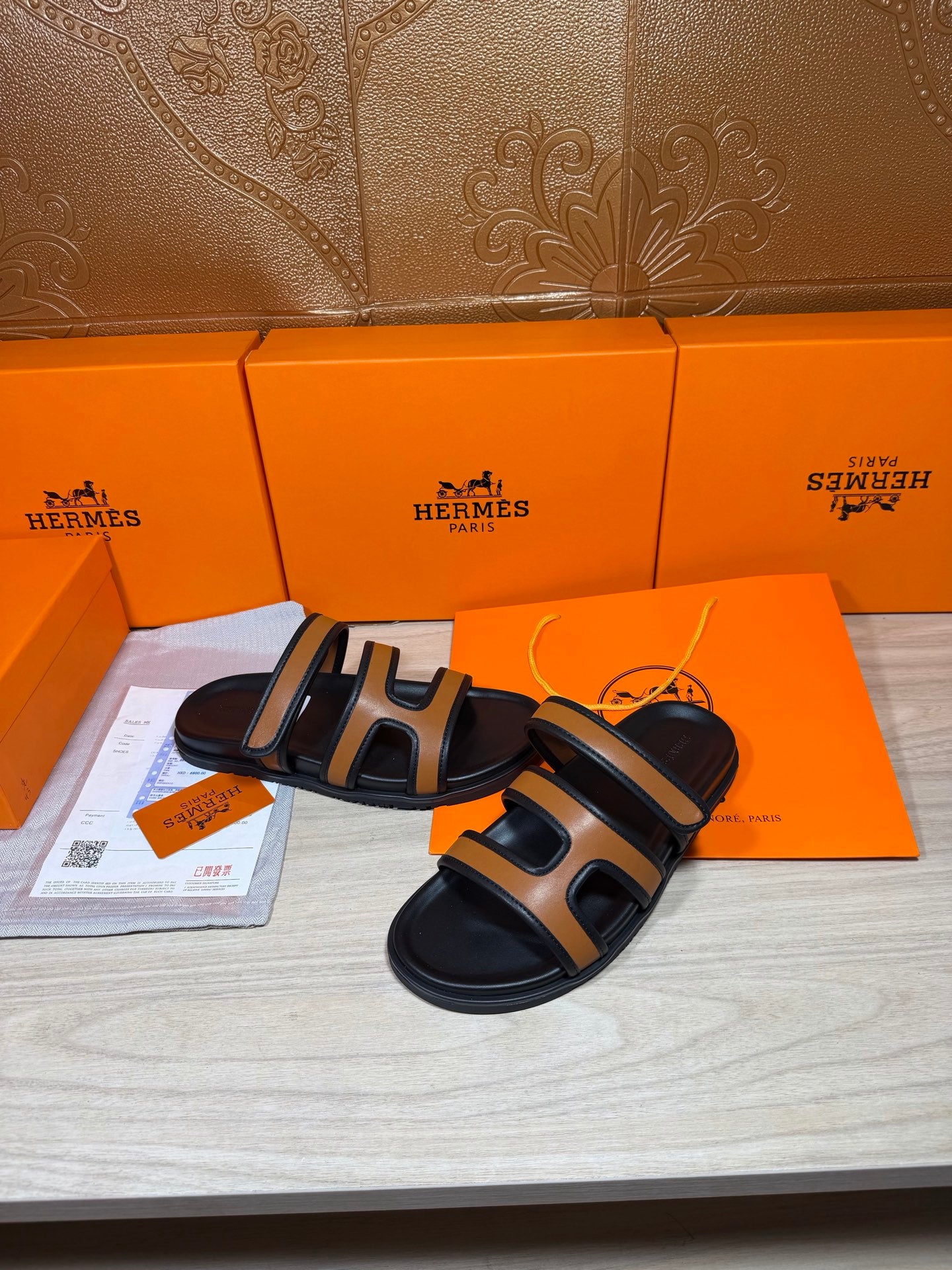 Black and tan leather slide sandals with two strap loops, paired on display