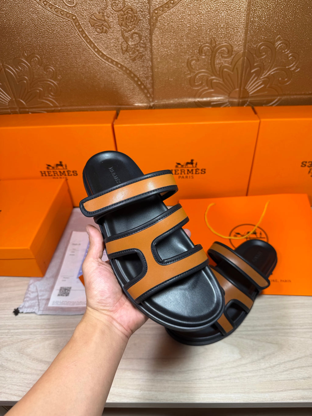 Handheld black and tan slide sandal with two strap bands and open toe