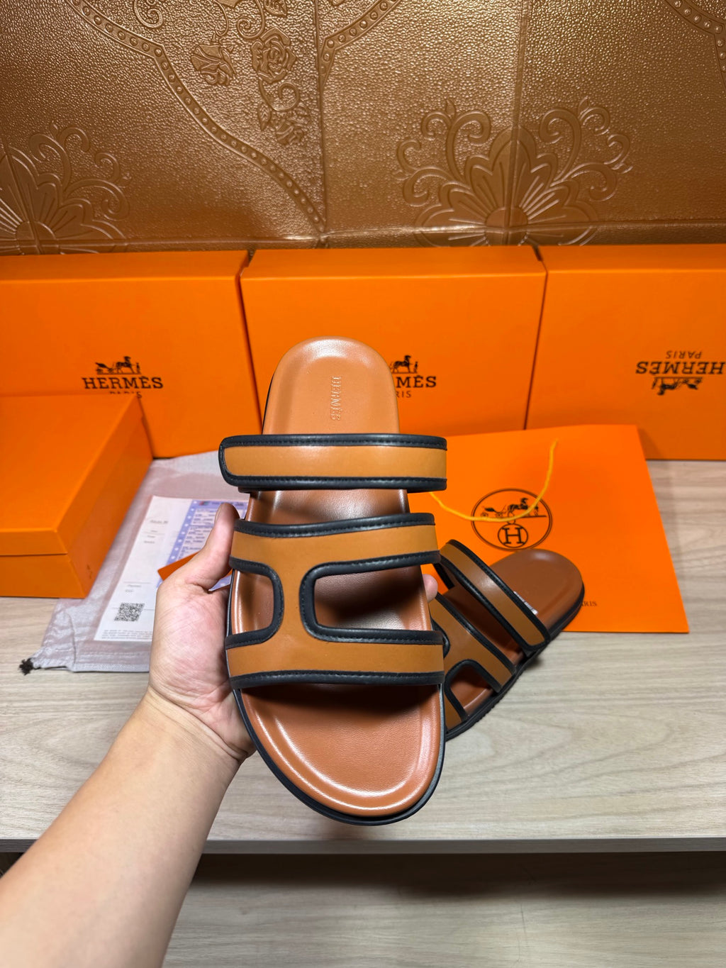 Hermes slide sandals held up, dark blue straps over tan footbed, close view