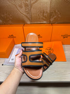 Hermes slide sandals held up, dark blue straps over tan footbed, close view