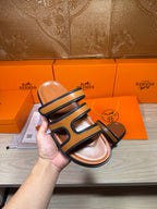 Hermes slide sandals held up by hand, dark blue straps and tan footbed