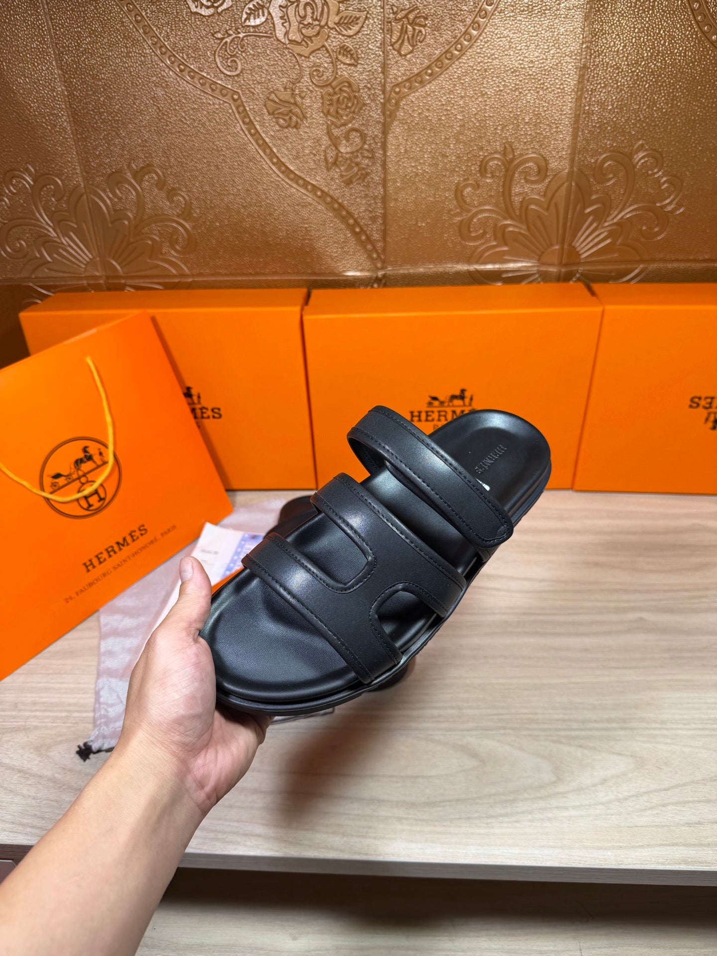 Hermes dark leather slide sandals with wide upper straps, held for a side view