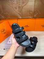 Hermes dark leather sandals with adjustable-looking two-strap upper, held in hand