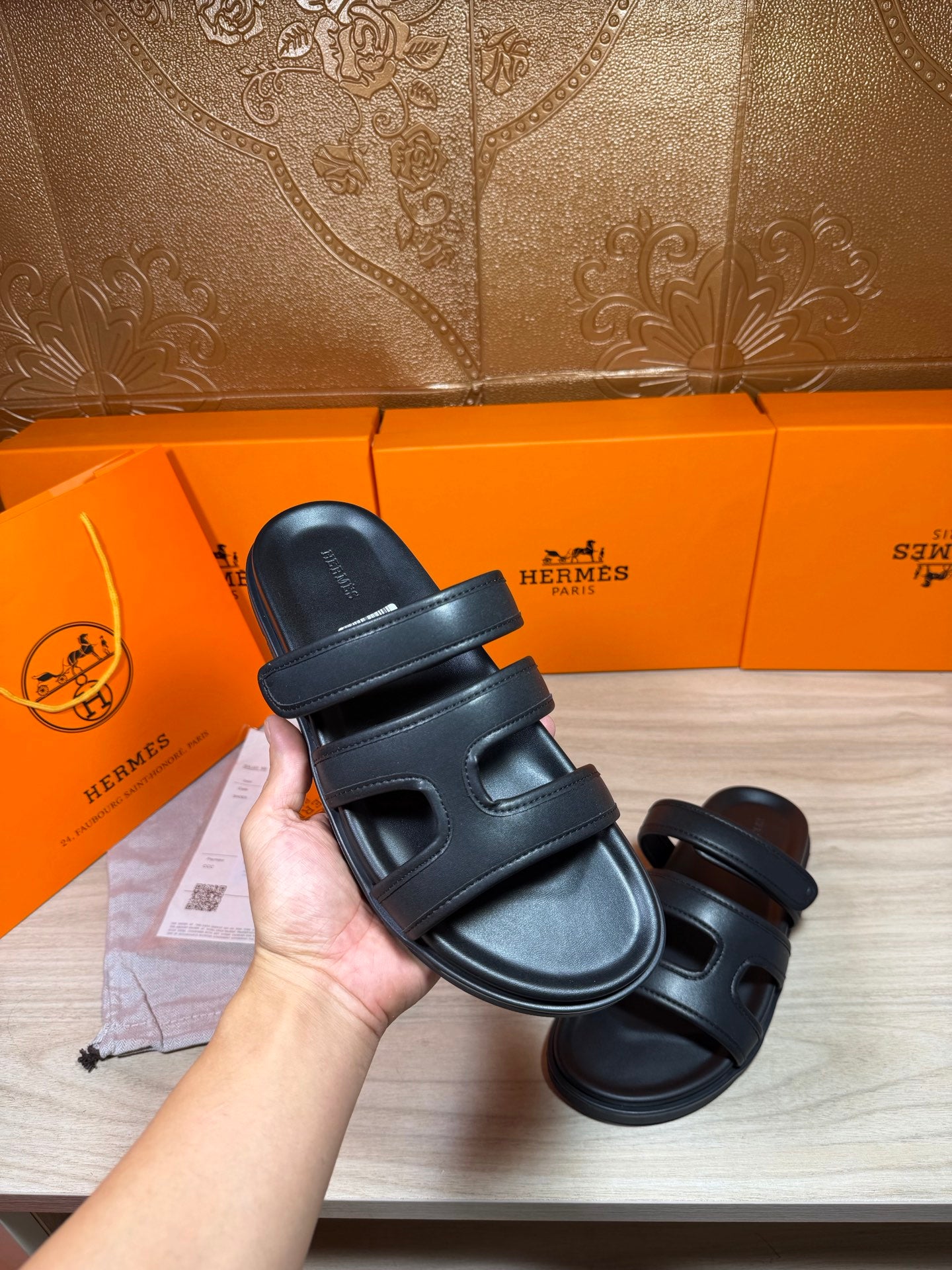 Hermes dark leather sandals with adjustable-looking two-strap upper, held in hand