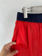 Moncler red shorts with navy waistband; hand holding the side seam and hem