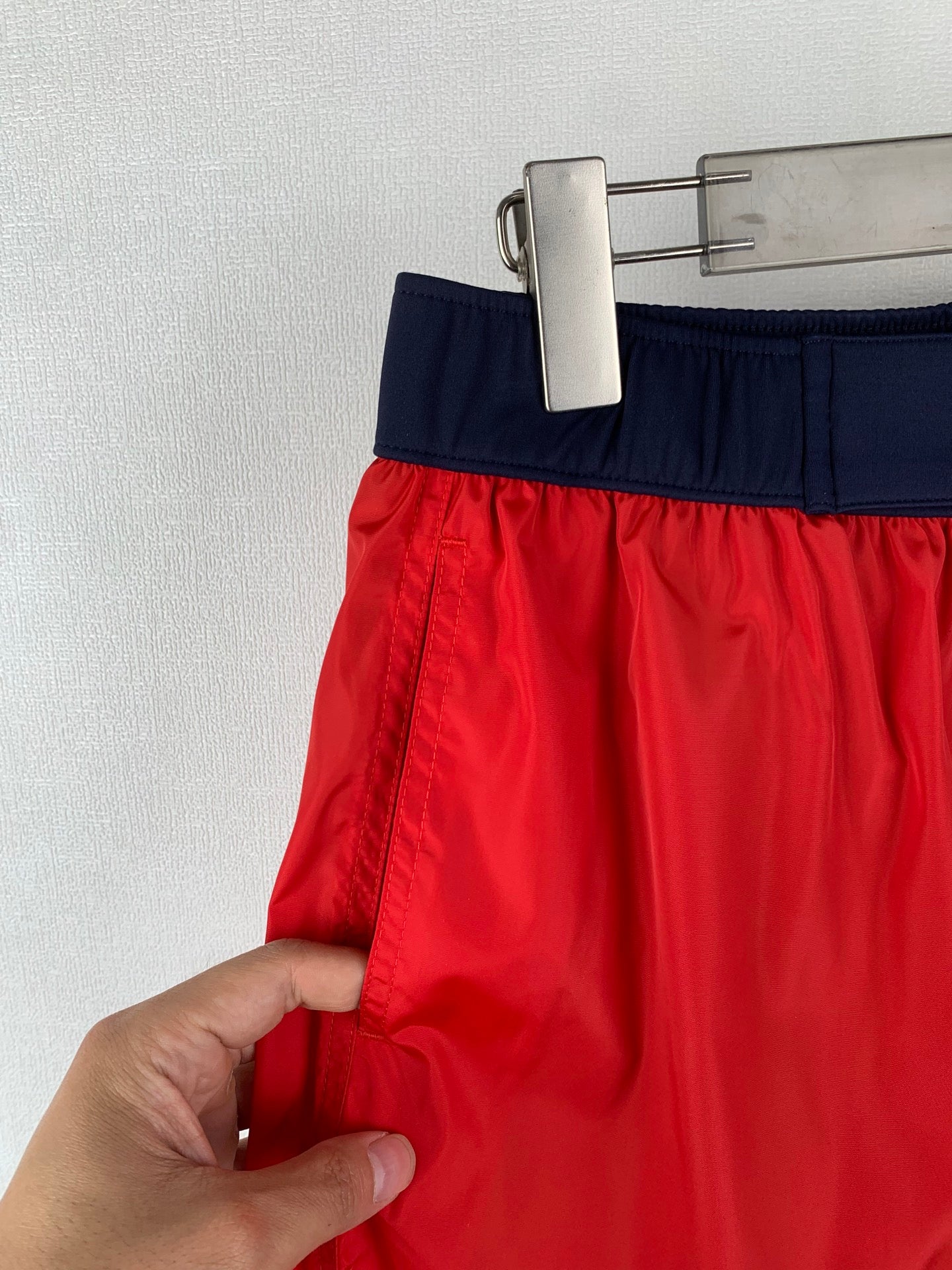 Moncler red shorts with navy waistband; hand holding the side seam and hem