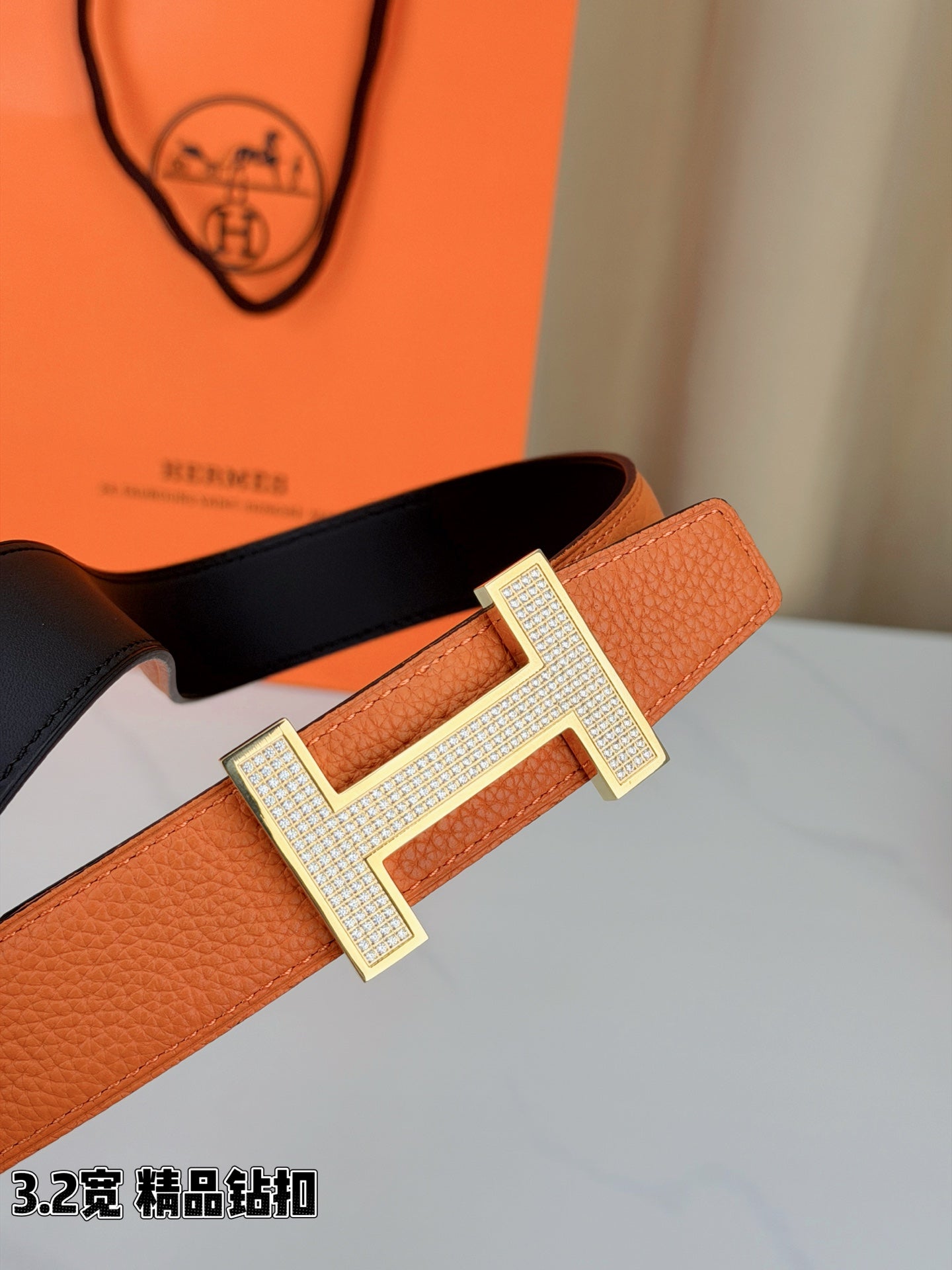 Hermes belt close-up: orange strap with silver H buckle and dark backing