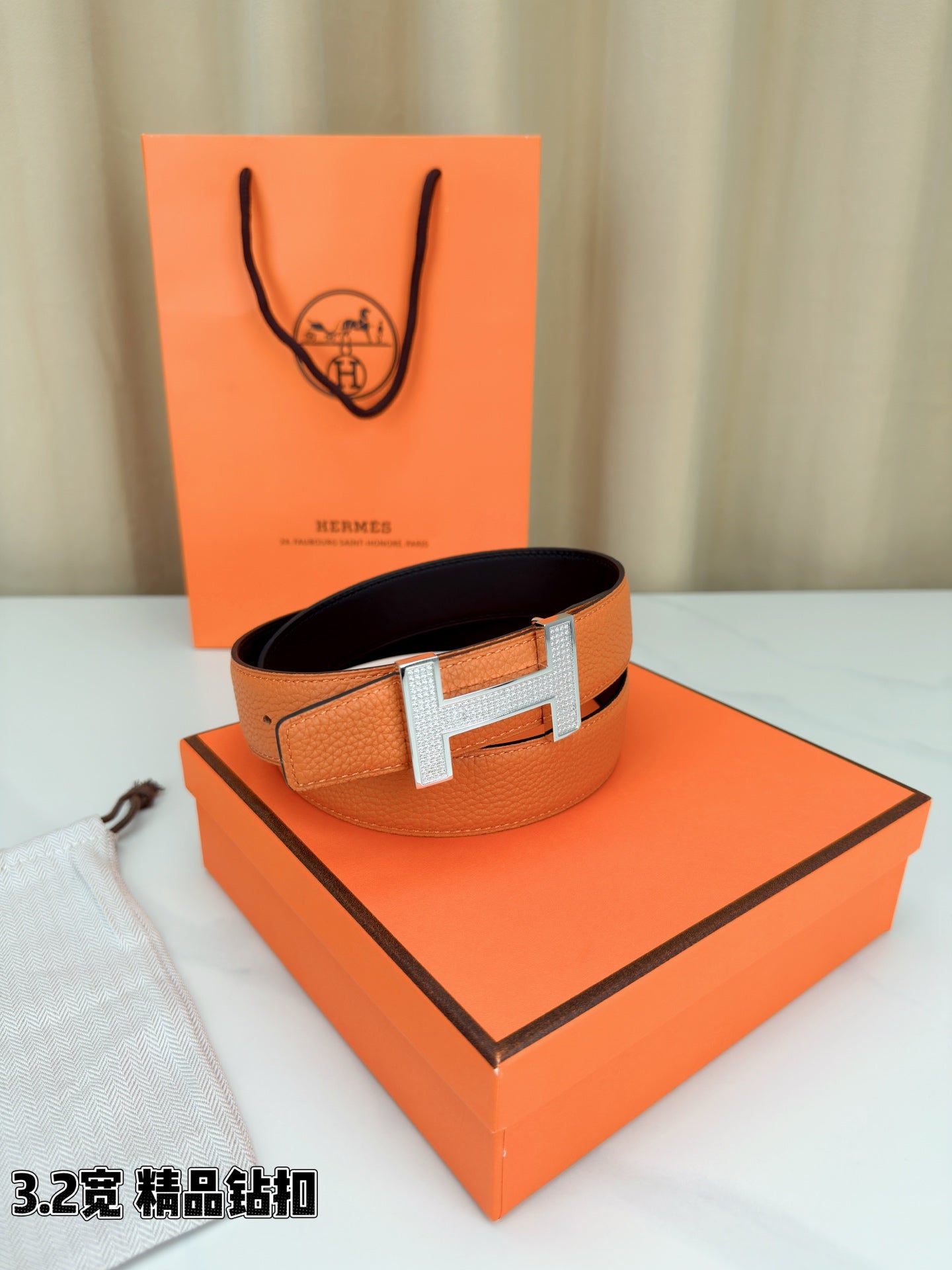 Hermes belt with orange leather and silver H buckle, angled view