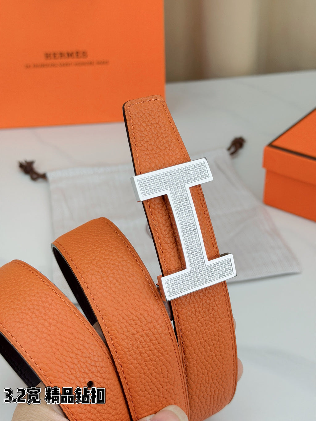 Hermes belt leather close-up: orange textured strap with silver H buckle