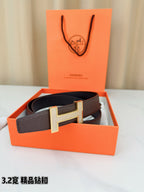Dark brown leather belt with gold-tone H buckle resting in a box