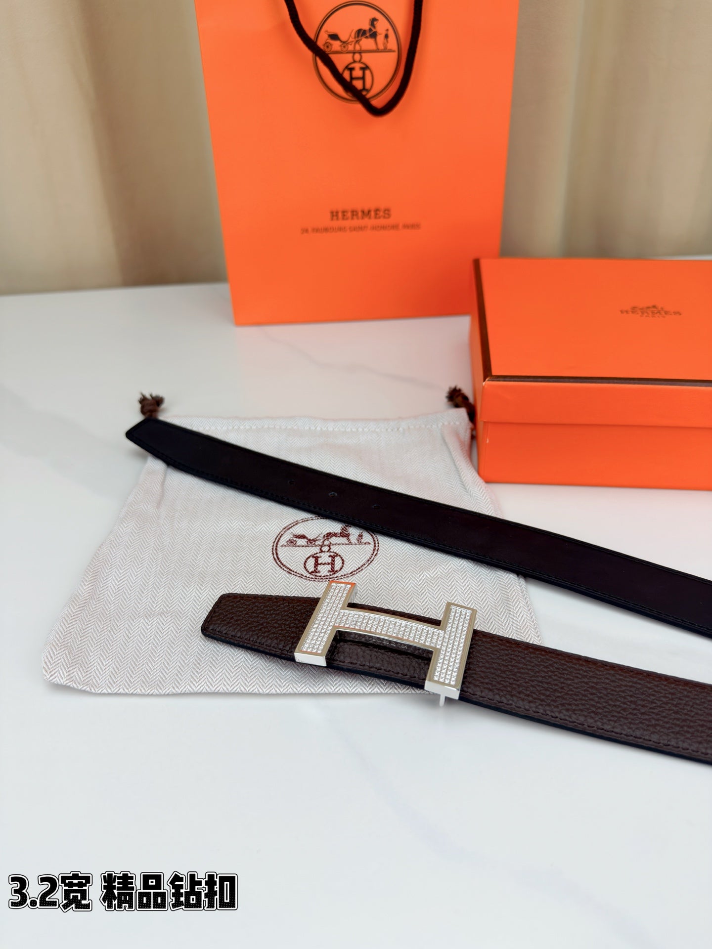 Dark brown leather belt with gold-tone H buckle laid across a cloth