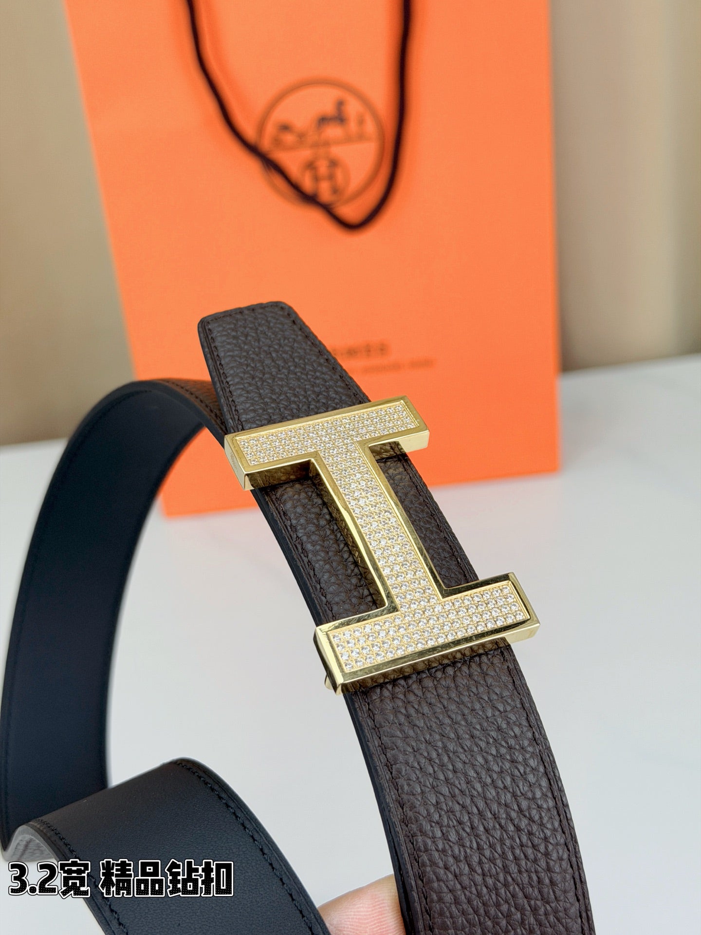 Dark brown leather belt buckle close-up with gold-tone H clasp and sparkle details