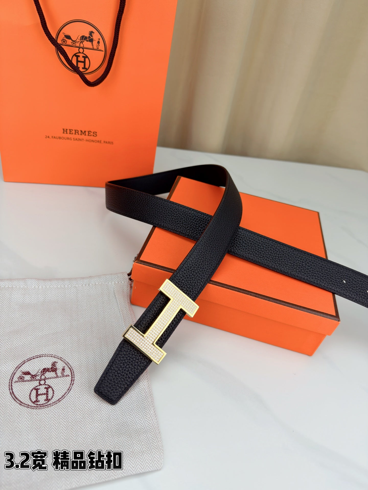 Hermes belt with dark leather strap and silver-tone H buckle, resting on packaging