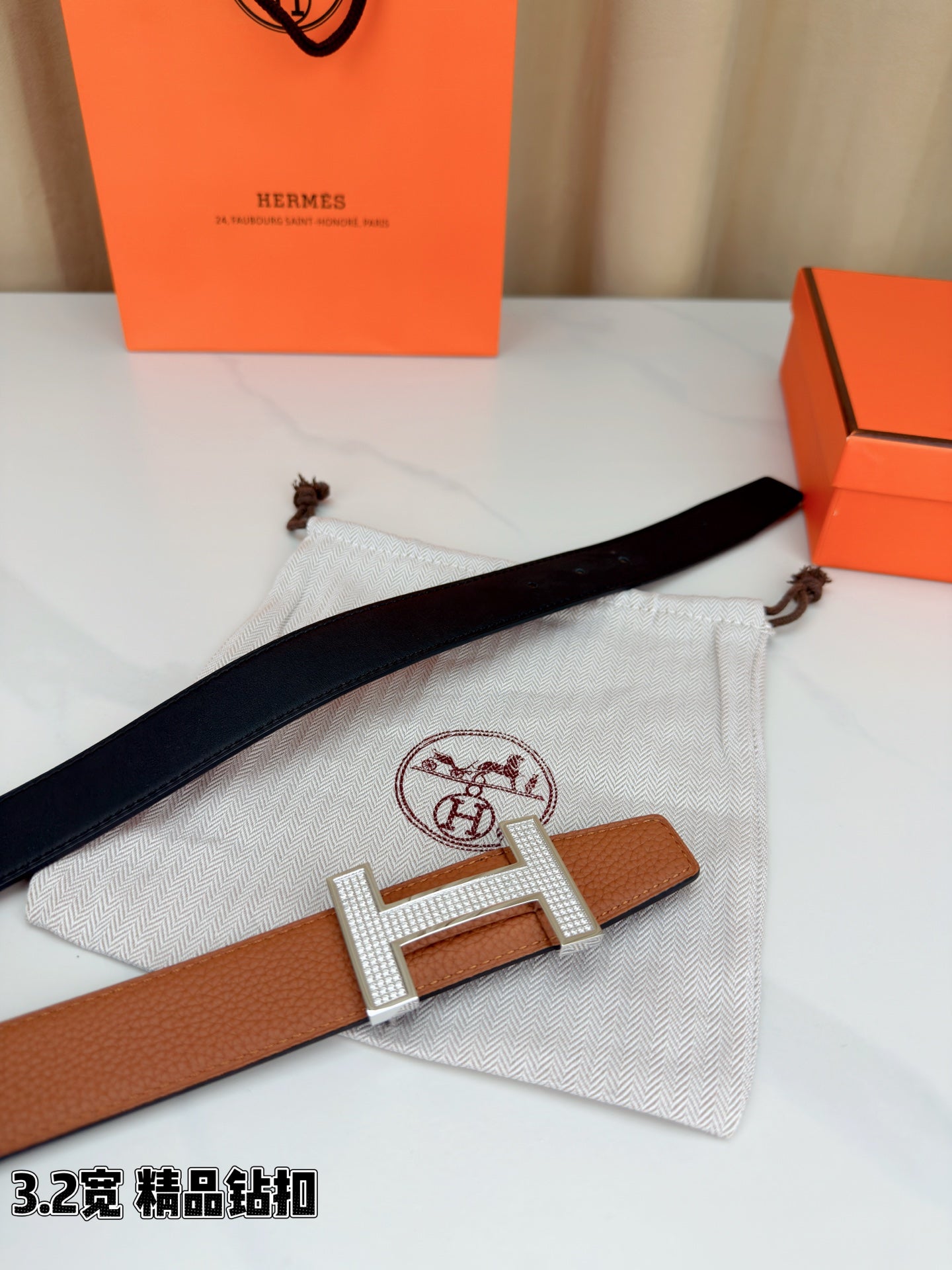 Tan leather belt with silver H buckle on black strap section, laid across fabric