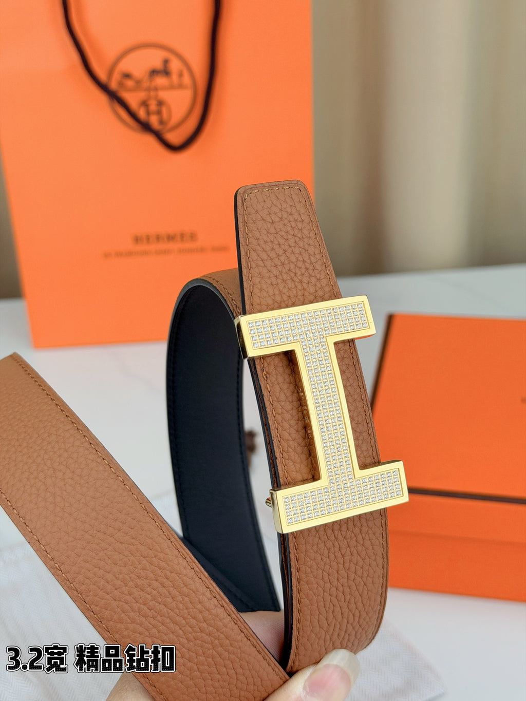 Close-up of tan belt with silver H buckle on pebble-grain leather strap