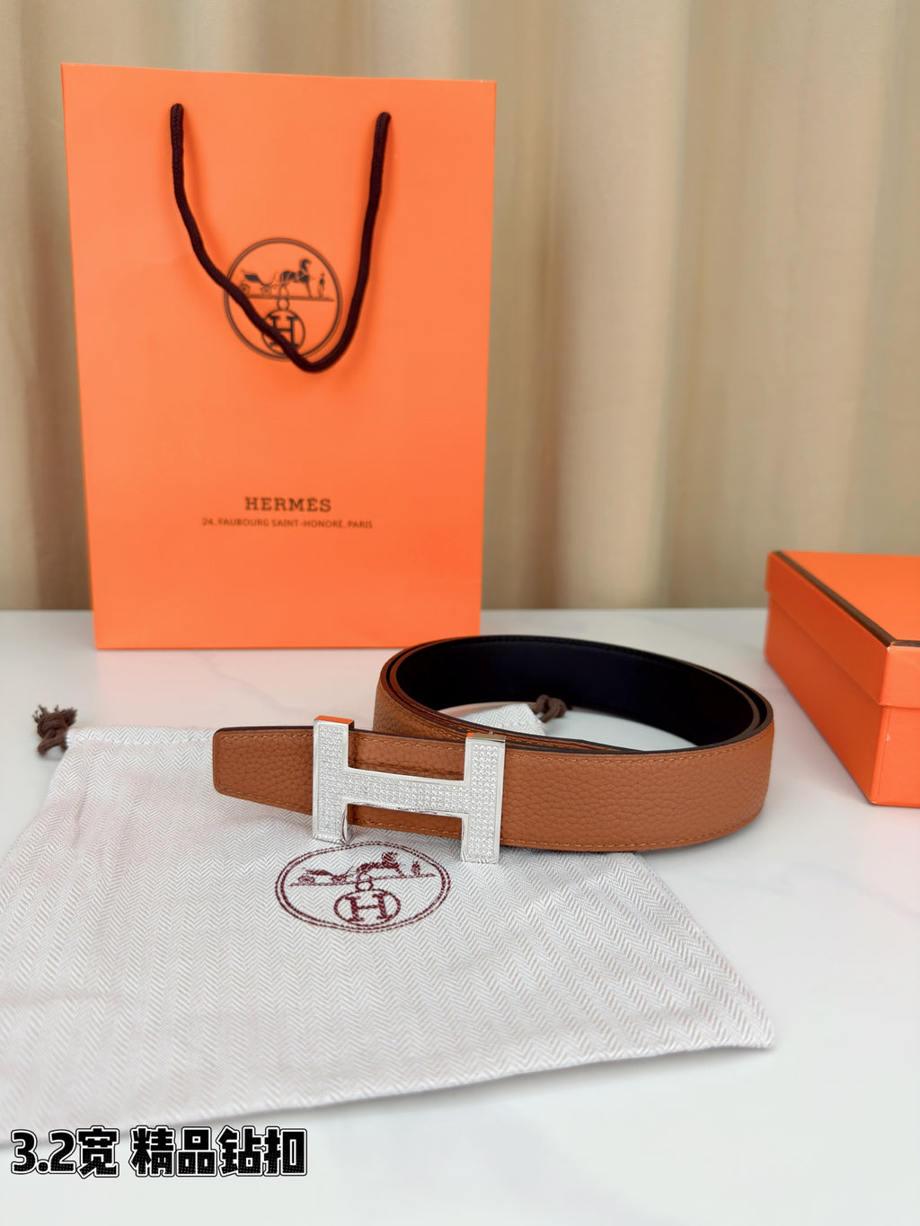 Tan leather belt with silver H buckle, laid flat with box and dust bag nearby