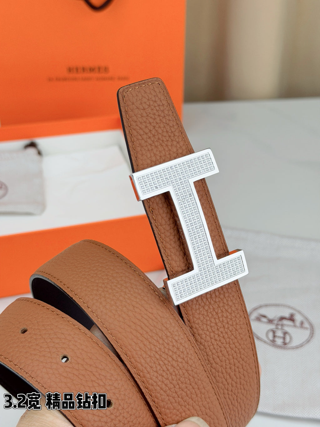 Close-up of tan leather belt with silver H buckle and pebbled texture