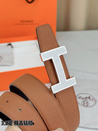 Close-up of tan leather belt with silver H buckle and pebbled texture