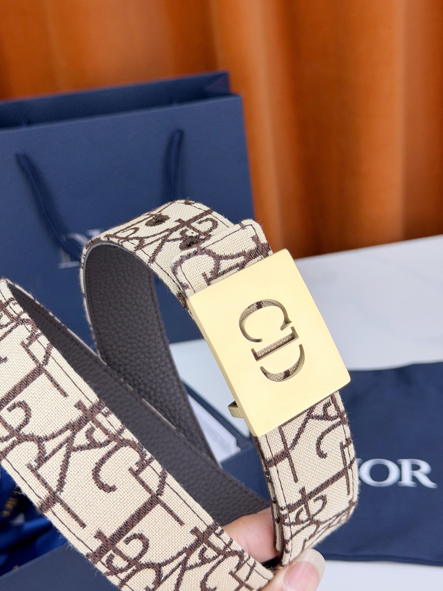 Dior belt close-up: beige monogram strap, dark edges, gold-tone 'CD' buckle
