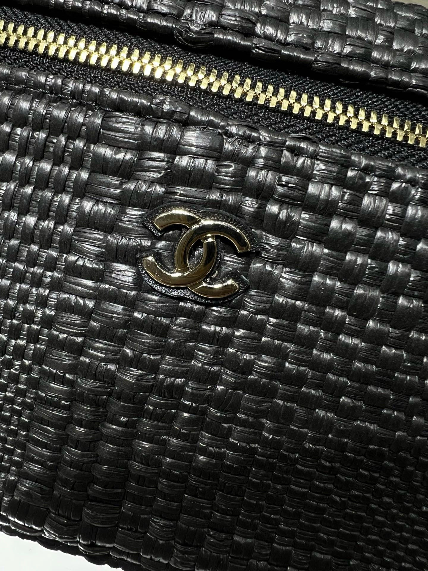 Black woven handbag with Chanel CC logo and gold-tone zipper detail, close-up