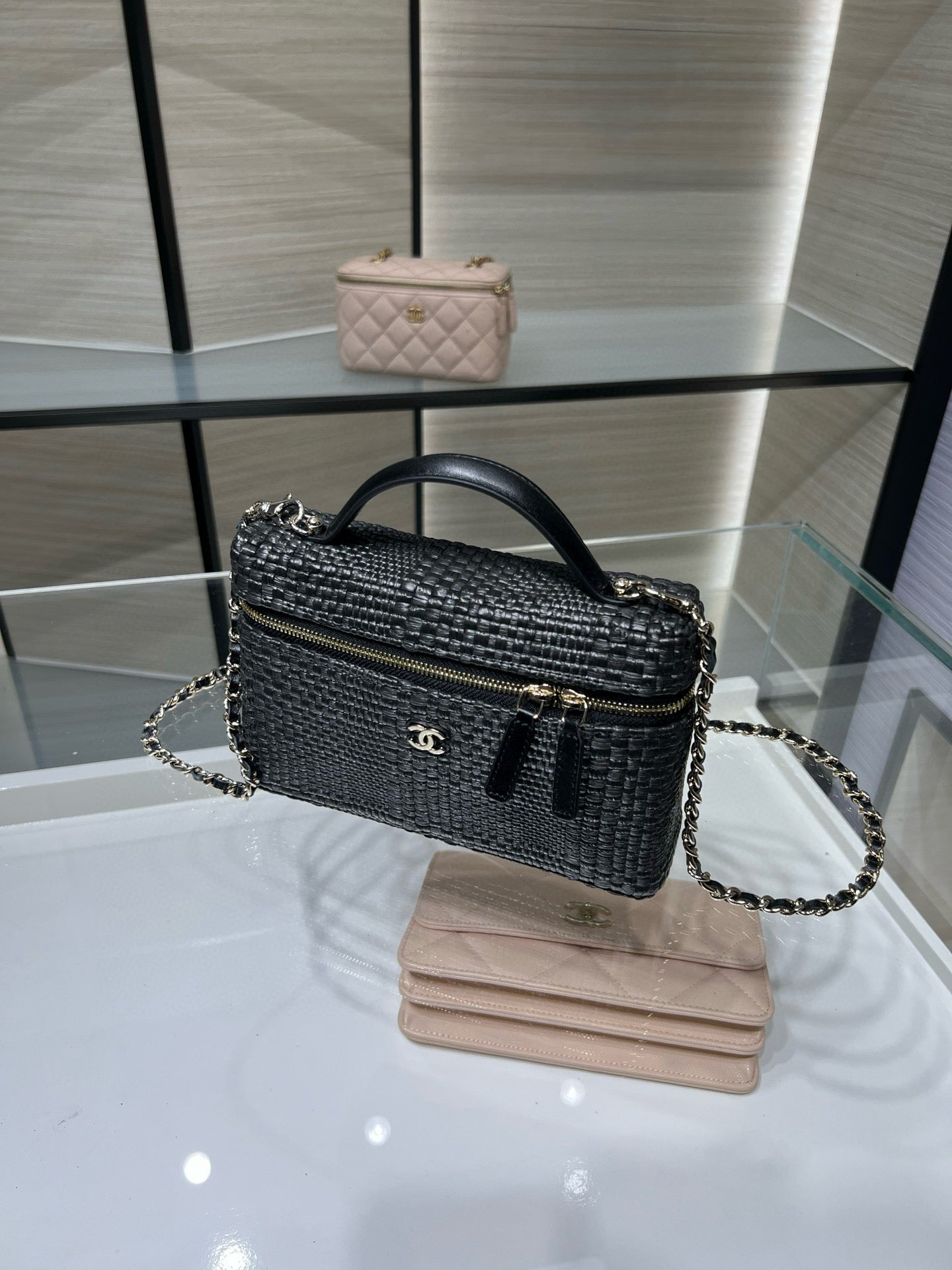 Black woven handbag with top handle, chain strap, and gold zipper closure, front