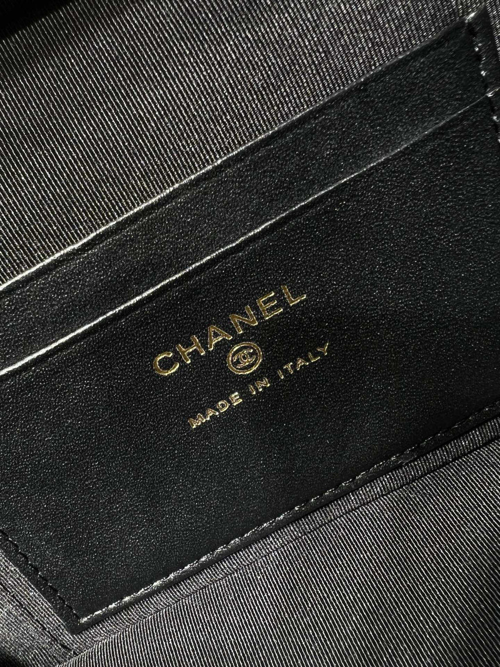 Black leather label on handbag reading CHANEL Made in Italy, gold lettering