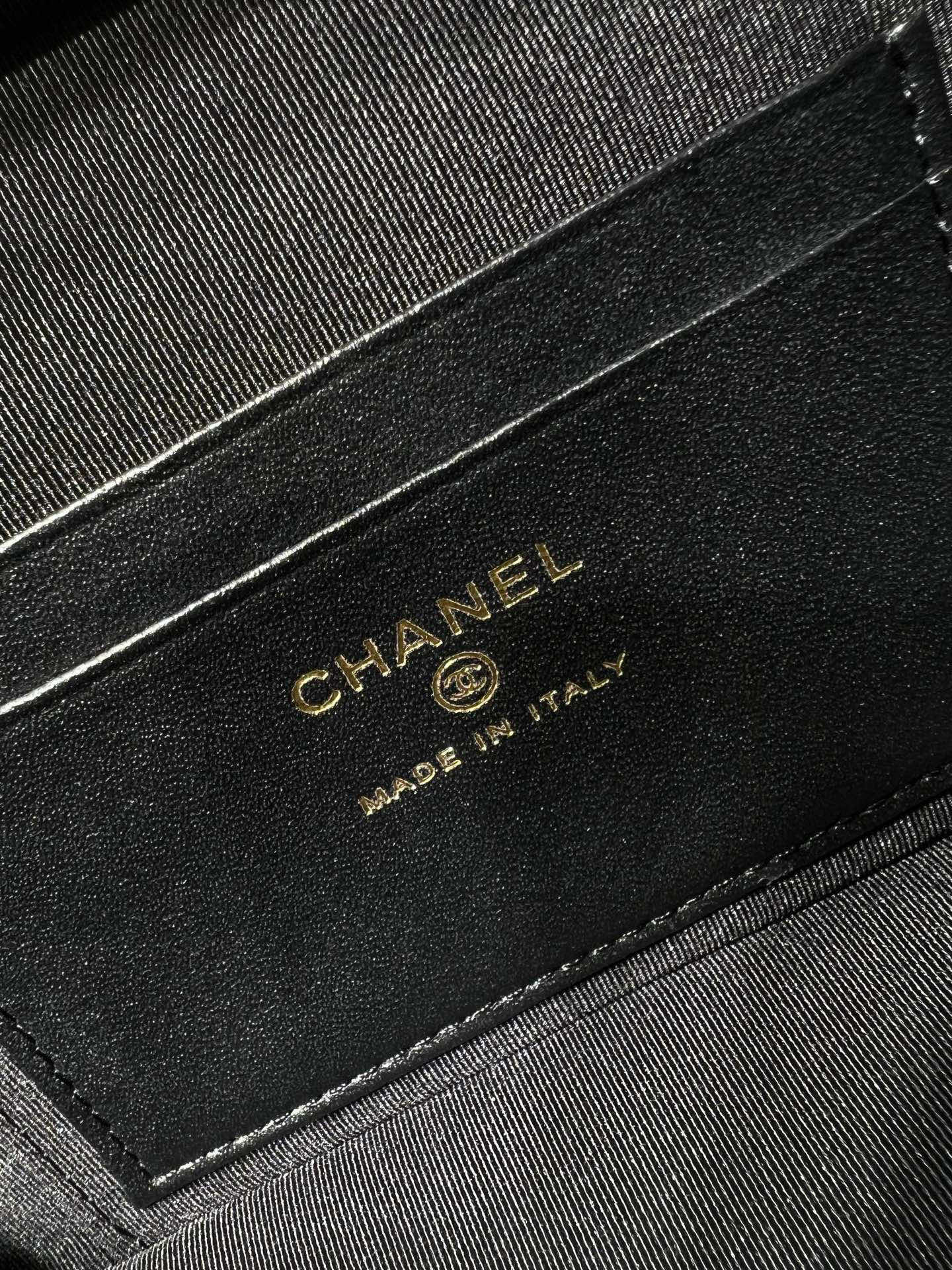 Black leather label on handbag reading CHANEL Made in Italy, gold lettering