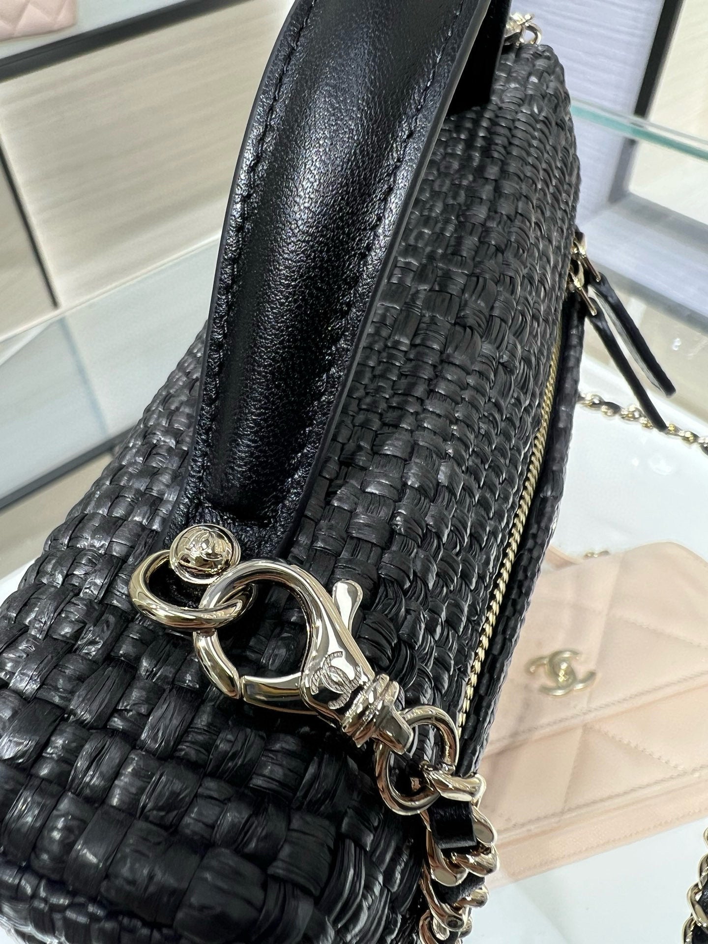 Black woven shoulder bag with wide leather strap panel and chain hardware, side view