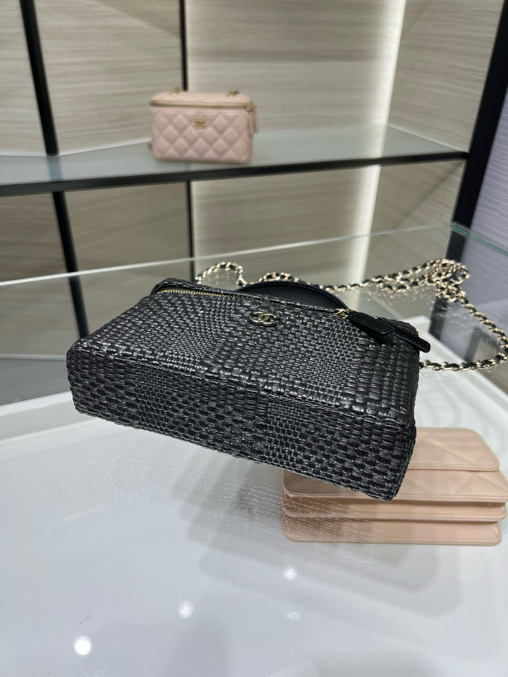 Black woven mini crossbody bag with chain strap and gold zipper trim, angled view
