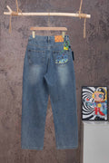 Blue denim pants with Louis Vuitton graphic patch on back pocket, hanging on wooden hanger.