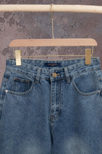 Light blue denim jeans with front pockets and belt loops, Louis Vuitton logo at center.