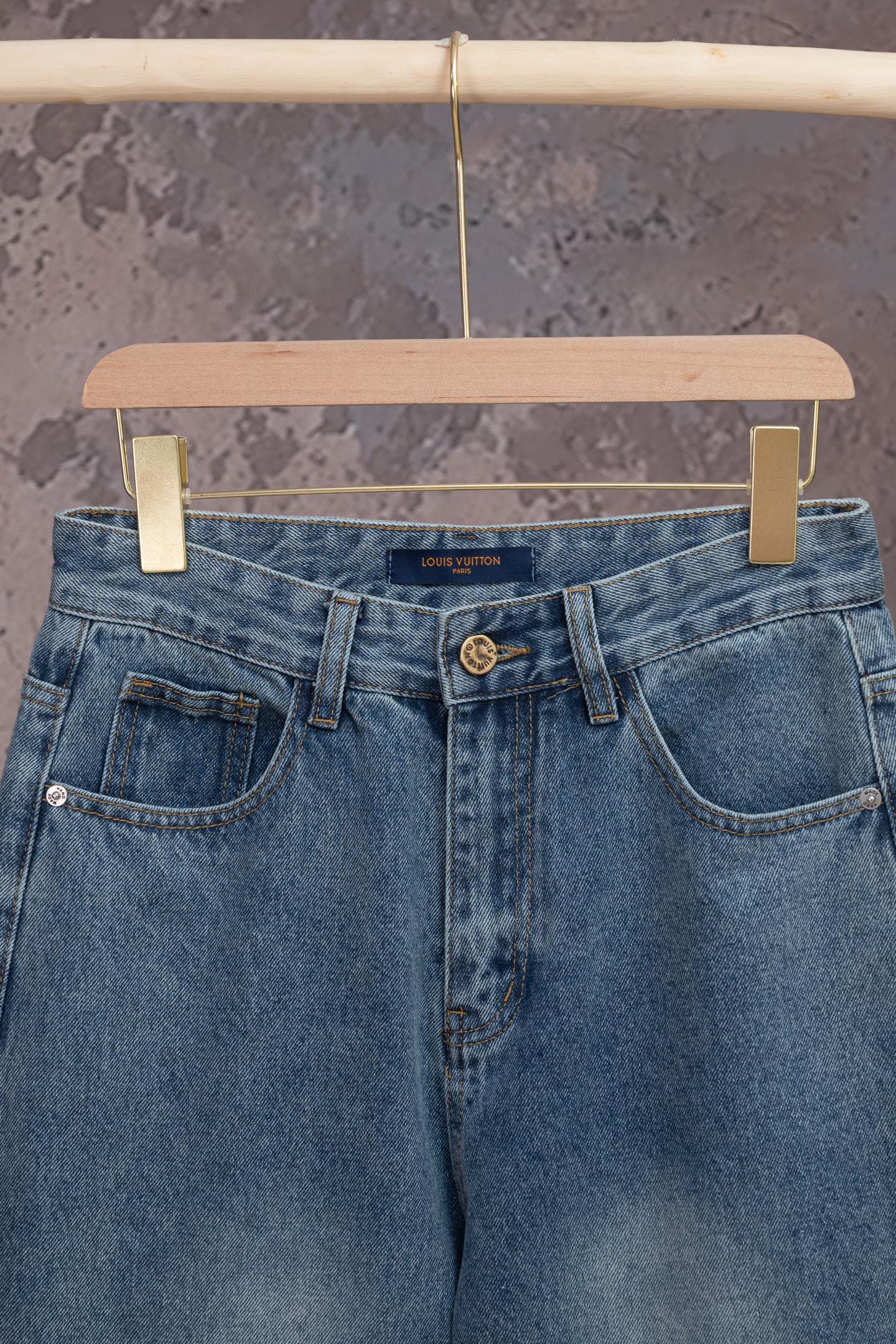Light blue denim jeans with front pockets and belt loops, Louis Vuitton logo at center.